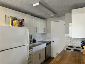 Kitchen featuring backsplash, butcher block countertops, white appliances, and white cabinetry