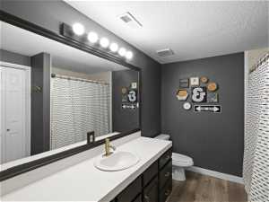Bathroom with a textured ceiling, wood-style floors, vanity, and toilet