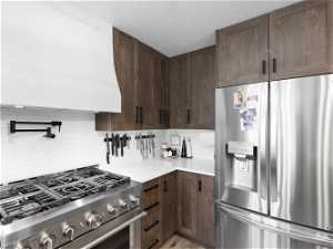 Kitchen featuring dark brown cabinets, appliances with stainless steel finishes, backsplash, and custom range hood