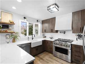 Kitchen with stainless steel appliances, custom range hood, a textured ceiling, sink, and light wood-type flooring
