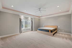 Unfurnished bedroom with ceiling fan, ornamental molding, a tray ceiling, and light carpet