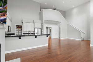 Kitchen featuring a towering ceiling, kitchen peninsula, white cabinets, and appliances with stainless steel finishes