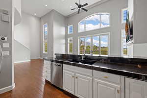 Kitchen with a towering ceiling, stainless steel dishwasher, dark wood-type flooring, sink, and white cabinetry