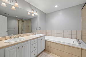 Bathroom featuring tile flooring, independent shower and bath, double sink, and vanity with extensive cabinet space