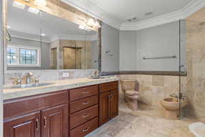 Bathroom featuring a shower with shower door, a bidet, tile walls, dual vanity, and toilet