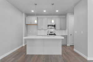 Kitchen with pendant lighting, a kitchen island with sink, stainless steel appliances, and light wood-type flooring