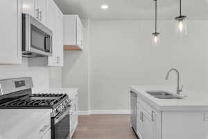 Kitchen with decorative light fixtures, stainless steel appliances, sink, and white cabinets