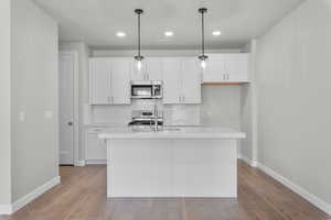 Kitchen featuring appliances with stainless steel finishes, decorative light fixtures, white cabinetry, and a kitchen island with sink