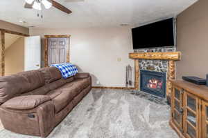 Living room featuring a stone fireplace, ceiling fan, carpet floors, and a textured ceiling