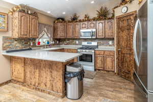 Kitchen featuring sink, kitchen peninsula, backsplash, and appliances with stainless steel finishes