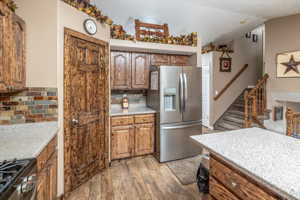 Kitchen featuring stove, light wood-type flooring, light stone counters, stainless steel refrigerator with ice dispenser, and tasteful backsplash