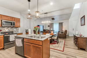 Kitchen featuring an island with sink, ceiling fan, stainless steel appliances, and light hardwood / wood-style floors