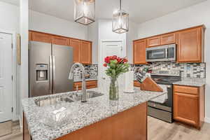 Kitchen with a kitchen island, light hardwood / wood-style flooring, stainless steel appliances, pendant lighting, and tasteful backsplash