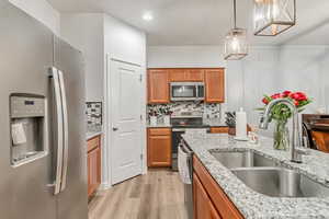 Kitchen with light stone counters, light hardwood / wood-style floors, stainless steel appliances, hanging light fixtures, and sink