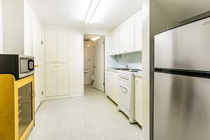 Basement Kitchen with stainless steel appliances, white cabinets, and light tile flooring