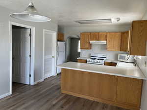 Kitchen featuring kitchen peninsula, dark wood-type flooring, sink, white appliances, and a textured ceiling