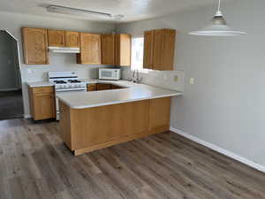 Kitchen with white appliances, kitchen peninsula, wood-type flooring, pendant lighting, and sink