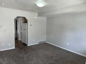 Unfurnished room featuring a textured ceiling and dark colored carpet