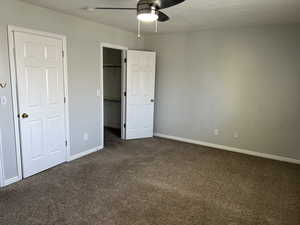 Unfurnished bedroom with dark colored carpet and ceiling fan