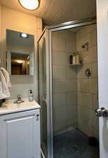 Bathroom with vanity, a shower with shower door, and a textured ceiling