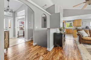 Living room featuring lofted ceiling, ceiling fan with notable chandelier, and light wood-type flooring