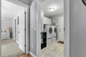 Washroom featuring washer and dryer, cabinets, a textured ceiling, and light tile flooring