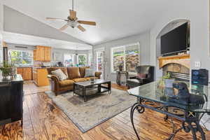 Living room with high vaulted ceiling, light hardwood / wood-style floors, a tiled fireplace, and ceiling fan