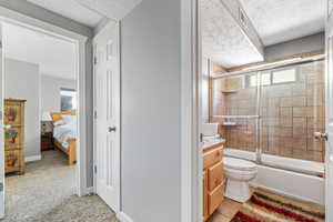 Full bathroom with a textured ceiling, vanity, toilet, and enclosed tub / shower combo