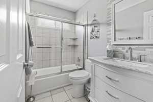 Full bathroom featuring tile flooring, enclosed tub / shower combo, vanity, and toilet