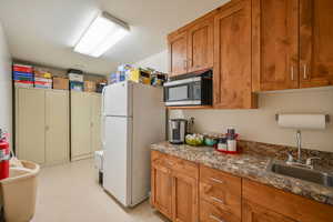 Kitchen with white refrigerator, sink, dark stone counters, and light tile flooring