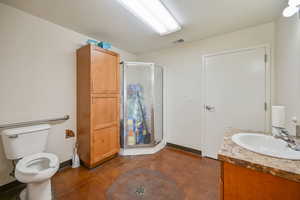 Bathroom featuring a shower with shower door, vanity, toilet, and concrete floors