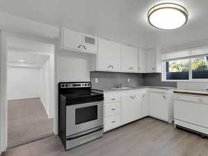 Kitchen with white dishwasher, white cabinets, electric range, backsplash, and light colored carpet