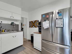 Kitchen with light hardwood / wood-style flooring, tasteful backsplash, sink, white cabinetry, and stainless steel refrigerator