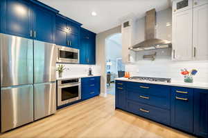 Kitchen featuring appliances with stainless steel finishes, tasteful backsplash, blue cabinetry, and wall chimney exhaust hood