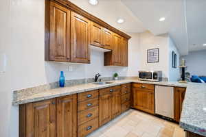 Basement kitchen with kitchen peninsula, light stone countertops, sink, and light tile floors