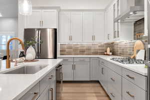 Kitchen featuring hanging light fixtures, light hardwood / wood-style flooring, appliances with stainless steel finishes, wall chimney exhaust hood, and tasteful backsplash