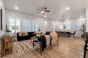 Living room with ceiling fan with notable chandelier and light wood-type flooring