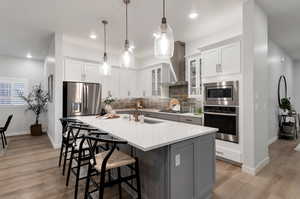 Kitchen with wall chimney exhaust hood, white cabinets, light wood-type flooring, and appliances with stainless steel finishes