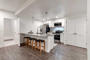 Kitchen featuring wood-type flooring, kitchen peninsula, white cabinets, and appliances with stainless steel finishes