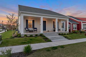 View of front facade with covered porch, central AC, and a lawn