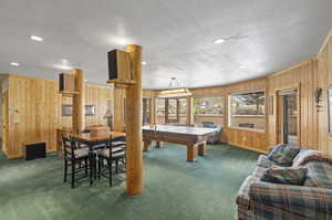 Recreation room with a textured ceiling, wood walls, and dark carpet, pool and ping pong table and game table