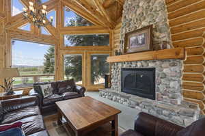 Living room with a fireplace, a notable chandelier, wood ceiling, high vaulted ceiling, and rustic walls