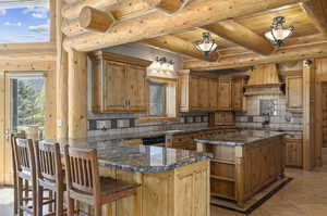 Kitchen with dark stone counters, light tile flooring, wood ceiling, premium range hood, and backsplash