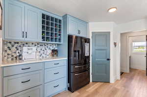 Kitchen with backsplash, blue cabinets, refrigerator, light wood-type flooring, and a textured ceiling