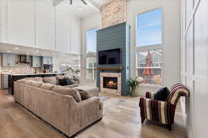 Living room featuring beamed ceiling, a towering ceiling, light hardwood / wood-style floors, and a stone fireplace