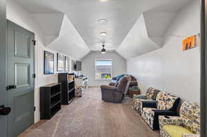 Living room featuring ceiling fan, vaulted ceiling, a textured ceiling, and carpet flooring