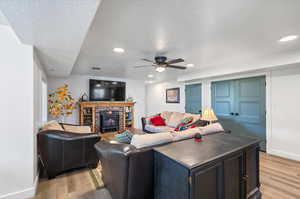 Apartment Living room featuring a brick fireplace, ceiling fan, light hardwood / wood-style floors, and a textured ceiling