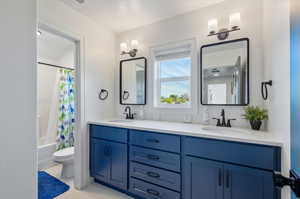 Full bathroom with large vanity, dual sinks, toilet, and shower / tub combo