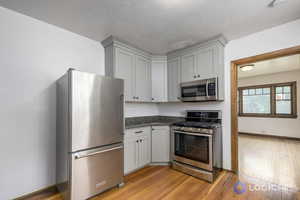 Kitchen featuring dark stone countertops, light hardwood / wood-style flooring, stainless steel appliances, and gray cabinetry