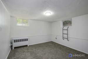 Basement with dark colored carpet, a textured ceiling, and radiator